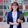 Portrait of confident female teacher mentor counselor social worker educator holding laptop inside library in educational building. Female professional education training sociology mental health